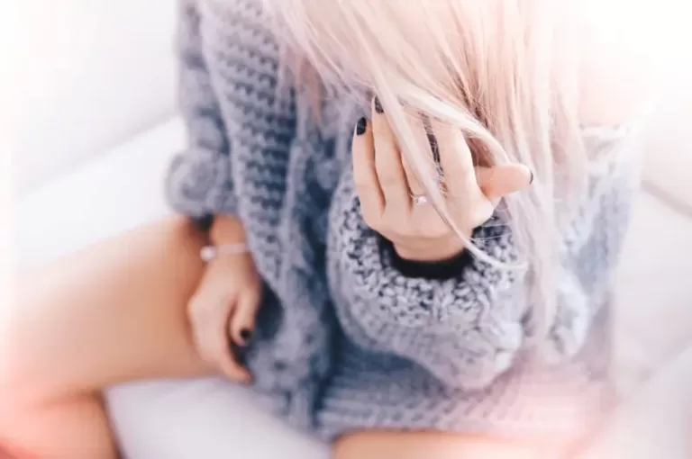 Femme assise jambes nues en pull, illustrant la gêne intime causée par une mycose vaginale