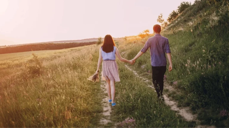 Couple vu de dos se tenant la main sur un chemin en pleine nature au coucher du soleil, symbole d'un projet de conception partagé