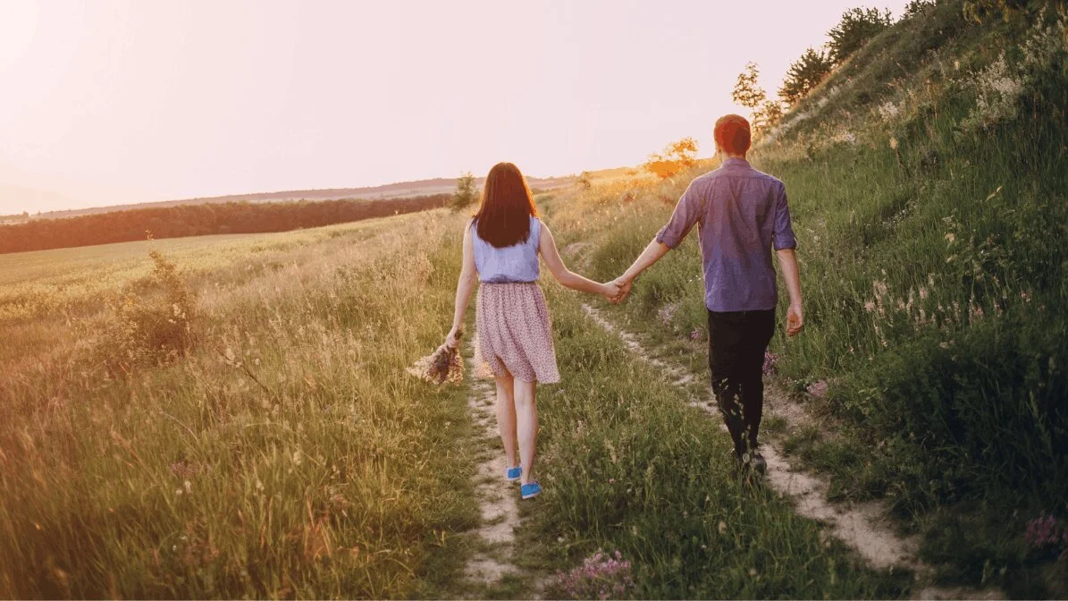 Couple vu de dos se tenant la main sur un chemin en pleine nature au coucher du soleil, symbole d'un projet de conception partagé